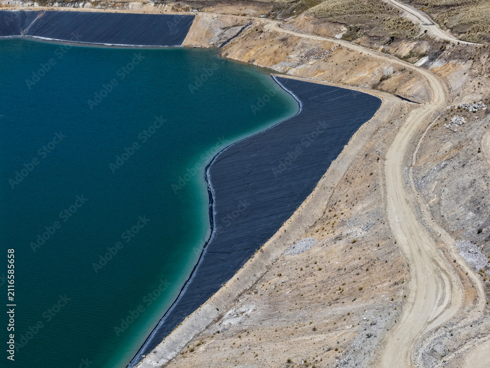 Fototapeta premium Tailings dam lined with HDPE geomembrane beside turquoise water and an access road seen from above