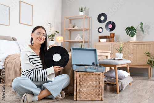 Beautiful woman with vinyl disk for record player sitting on floor in bedroom