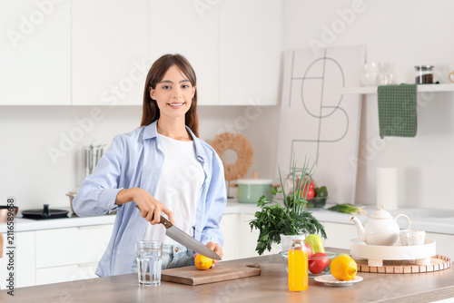Young woman cutting lemon at table in kitchen