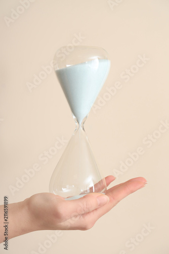 Quadro su tela Female hand holding hourglass on beige background