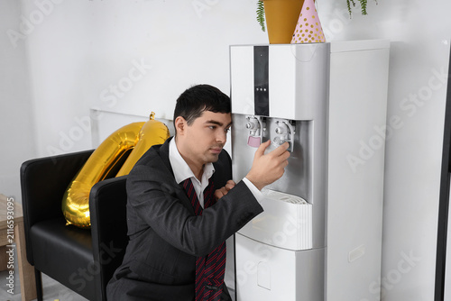 Hangover businessman pouring water from cooler after New Year party in office