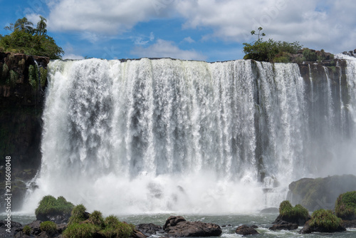 Bild auf Leinwand Majestic powerful waterfall cascading down rocky cliffs surrounded by lush green