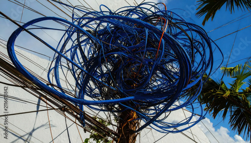 A Chaotic Tangle of Blue Electrical Wires and Cables Mounted on a Pole Against a Cloudy Sky