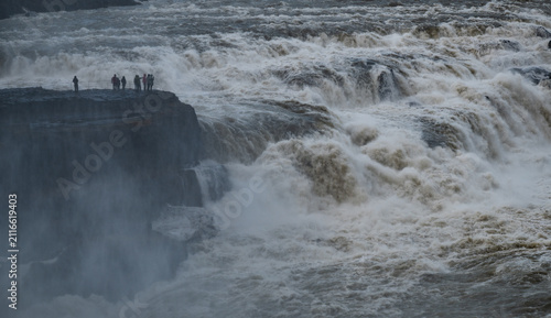 Obraz na płótnie Tourists standing on a cliff at gullfoss, experiencing the immense power of the golden waterfall and glacial river hvita