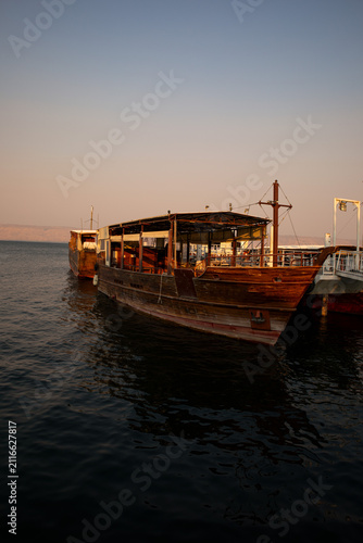 Fotografía Scenic Harbor View with Wooden Tourist Boat Anchored on the Sea of Galilee in Ti
