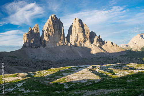 Tre Cime di Lavaredo. Iconic jagged peaks in the Italian Dolomites. Bathed in golden sunlight. Showcasing a stunning alpine summer landscape with partial shadows on the rugged terrain and green grass