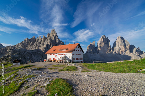 Rifugio Locatelli, a traditional alpine mountain hut, is situated under the iconic Tre Cime di Lavaredo peaks, offering hikers a resting point amidst the dramatic Dolomite Alps landscape in Italy