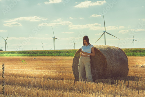 Konstfotografi A vintage portrait of a teenage girl finds a quiet moment in a nostalgic hayfield, absorbed in her smartphone