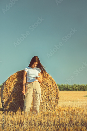 Fotografie A vintage portrait of a teenage girl finds a quiet moment in a nostalgic hayfield, absorbed in her smartphone