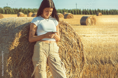 Canvastavla A vintage portrait of a teenage girl finds a quiet moment in a nostalgic hayfield, absorbed in her smartphone