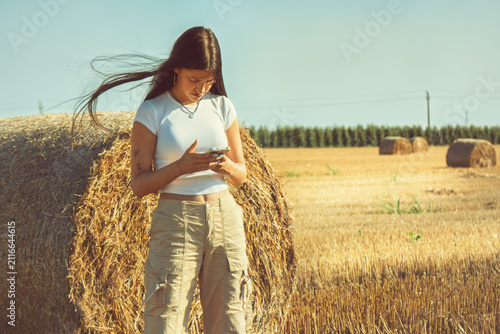 Konstfotografi A vintage portrait of a teenage girl finds a quiet moment in a nostalgic hayfield, absorbed in her smartphone