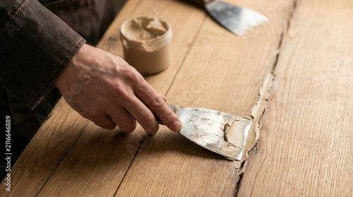 Male hand smoothing wood putty filler into wooden table crack, professional furniture restoration and repair
