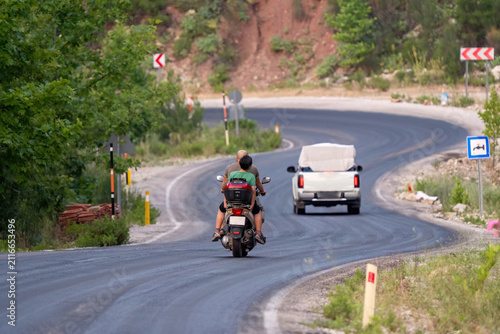Rear view of local residents commuting on a scooter along a curvy countryside road