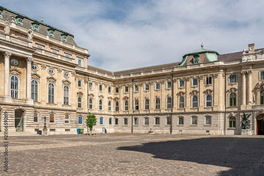 Obraz premium Wide cobblestone courtyard view of a long baroque wing of Buda Castle with rows of arched windows in Budapest, Hungary