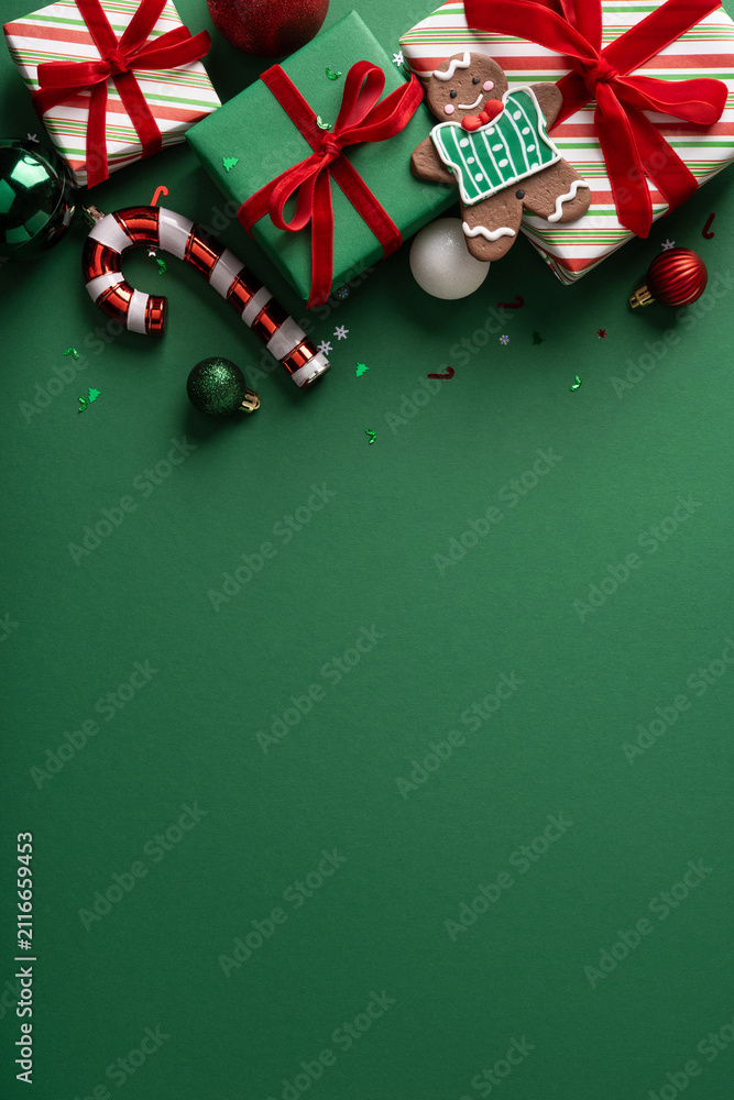 Obraz premium Christmas gifts with gingerbread cookie, red ribbons and ornaments on green vertical background for Merry Happy New Year