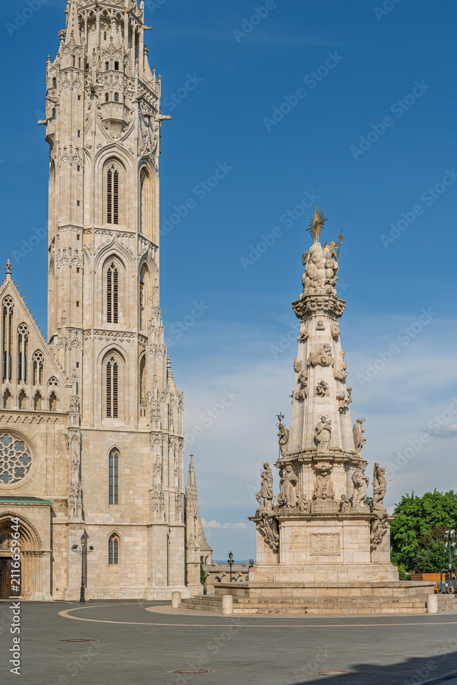 Fototapeta premium Tall Gothic tower of Matthias Church beside the Holy Trinity Statue on an empty plaza in Budapest, Hungary