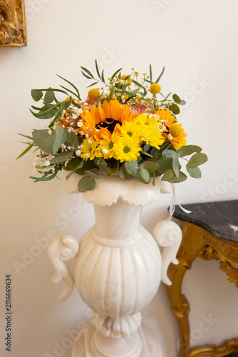 Bright flowers in a vase placed on a white pedestal in a room with golden decoration