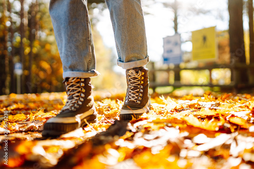 фотографія Female feet in hiking boots walk along a path strewn with fallen leaves