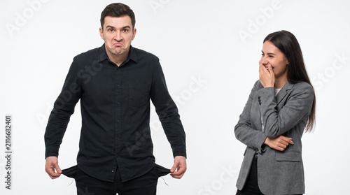 A man with empty pockets looking frustrated while a woman laughs beside him
