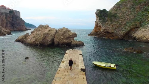 Aerial view of Kolorina Bay in Dubrovnik featuring the iconic stone pier, crystal clear Adriatic Sea and dramatic rocky coastline, a famous filming location from Game of Thrones.
