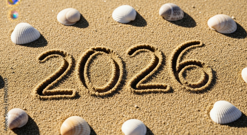New year twenty twenty six numbers written in sand beach texture with white sea shells framing festive seasonal date message for upcoming future.