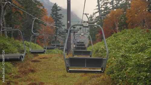 Empty chairlift moving over a vibrant autumnal forest on a foggy day at Daisetsuzan Sounkyo Kurodake Ropeway in Hokkaido, Japan. Beautiful scenery for tourism and travel in a famous national park