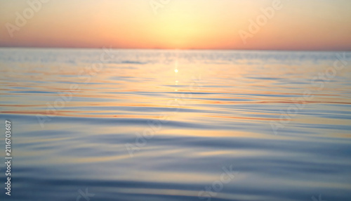 Ocean water surface ripples reflecting a warm golden sunset glow at twilight with soft focus blurred background horizon view