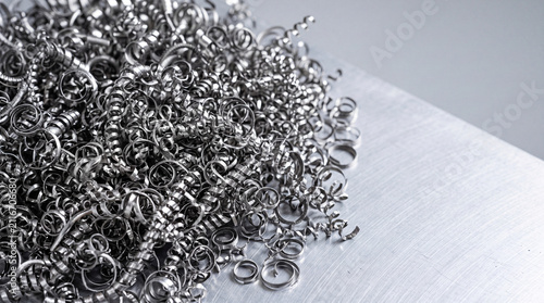 Metal shavings scattered on a metallic surface. The shavings are curly and shiny, showcasing the texture and color of the metal.