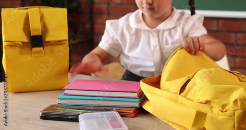 Little girl packing backpack at desk in school, closeup