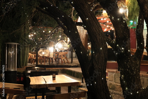 Cuadro en lienzo Terraza exterior de restaurante acogedor decorada con luces cálidas y mesas de m