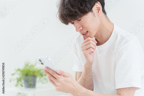悩みながらスマートフォンを使う若い男性