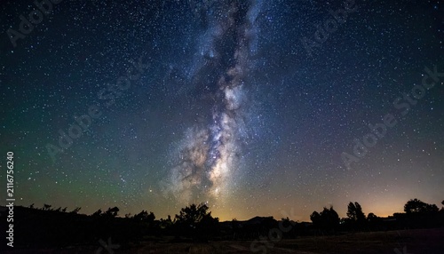 Vertical Milky Way galaxy band over forest treeline at night.