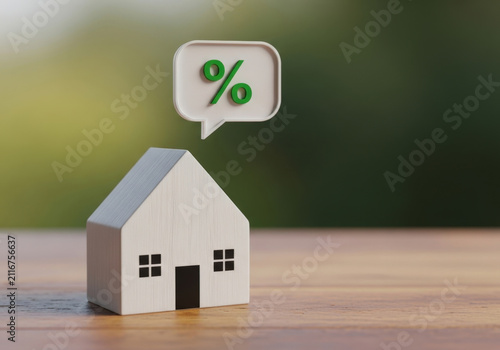 Small model house with white walls and black roof sitting on wooden table with speech bubble symbol displaying green percent sign finance concept.