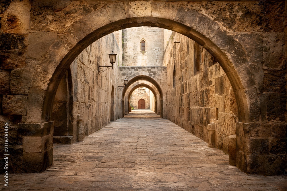 Fototapeta premium Historic Walkway Beneath Aged Stone Arches With Textured Walls Warm Light And Timeless Atmosphere Photography