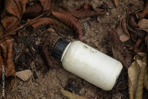 Foto Empty white plastic chemical bottle discarded among dry leaves on soil pollution