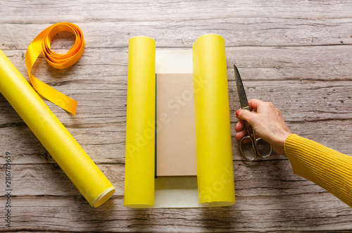 Woman cutting yellow wrapping paper on wooden table.