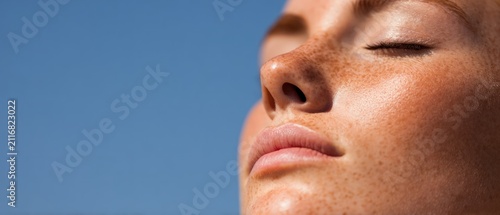 Close up portrait of young woman with freckles enjoying warm sunlight against clear blue sky natural skincare wellness concept