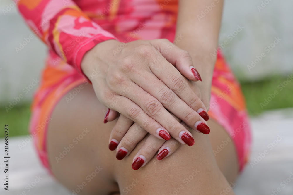 Fototapeta premium Close up of a woman's hands with painted red fingernails resting on her lap while wearing a colorful dress