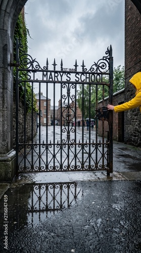 Person in Yellow Jacket Opening an Ornate Gate Back To School Environment
