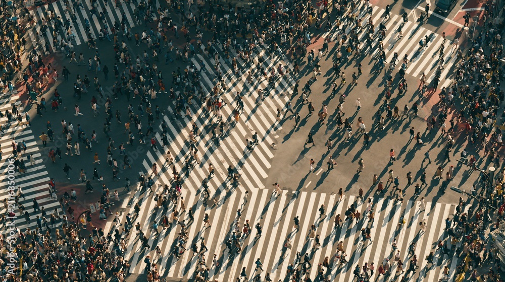 Fototapeta premium Aerial view of a massive crowd crossing a busy intersection with zebra stripes, capturing urban movement and city life energy.