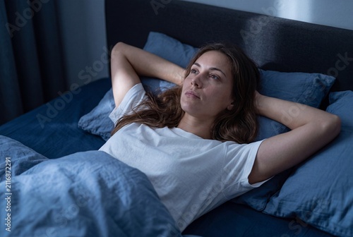 Young woman lying in bed awake at night, looking thoughtful and pensive