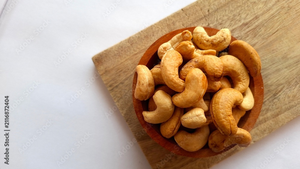 Fototapeta premium Photo of a collection of cashew nuts in a wooden bowl on a wooden cutting board