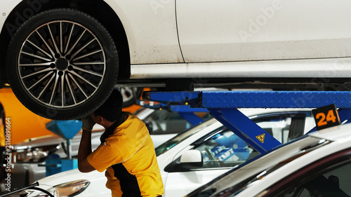 Auto mechanic inspecting vehicle under raised car in modern automotive service garage