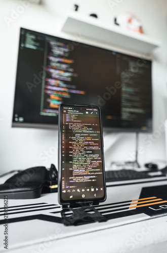Professional software engineering desk with large display, smartphone showing code and organized equipment. Comfortable workstation reflects efficient programming, testing and digital innovation.