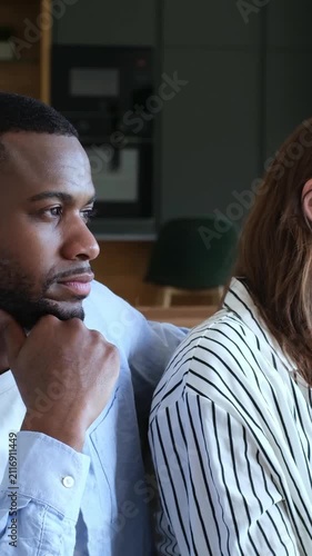 Young frustrated multiracial couple sitting back to back on the sofa, feeling sad and resentful after a fight, avoiding conversation and experiencing a difficult moment in their relationship