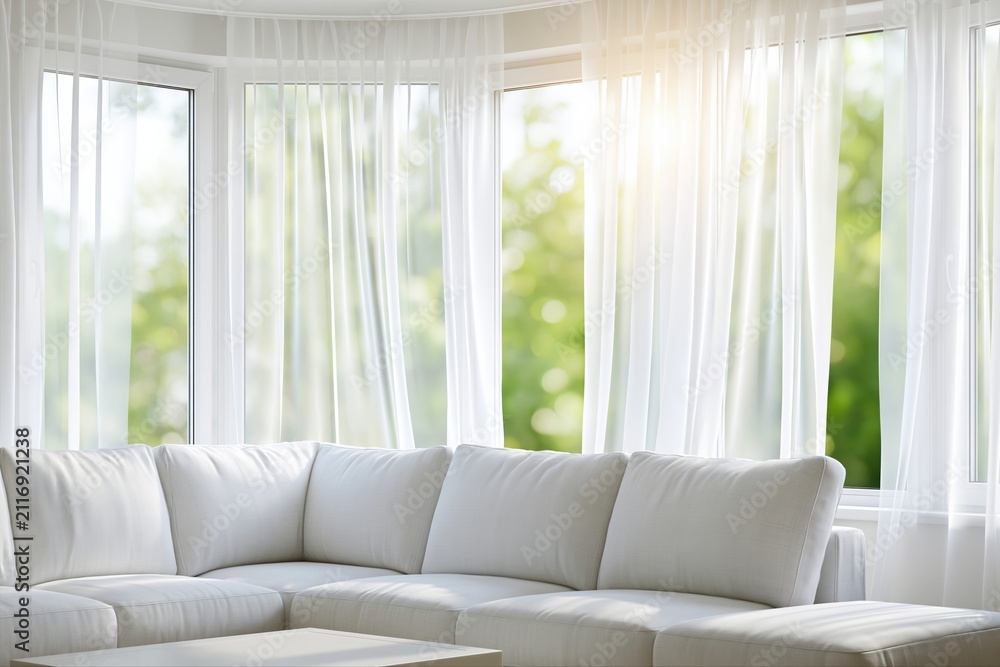 Obraz premium Bright and airy modern living room with white sofa and sheer curtains looking out onto a green garden