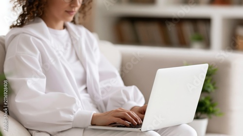 Young woman wearing comfortable loungewear working on laptop computer while relaxing on sofa at home