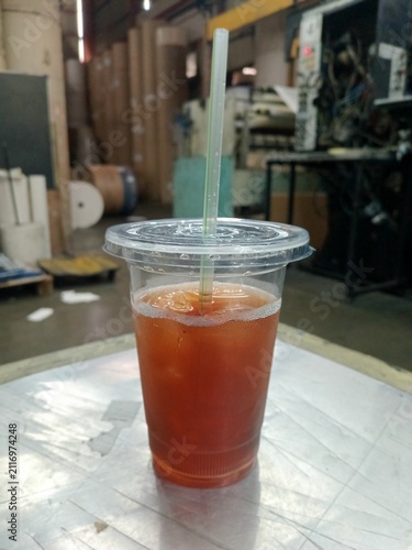 Iced tea in a clear plastic disposable cup with straw on table in factory setting