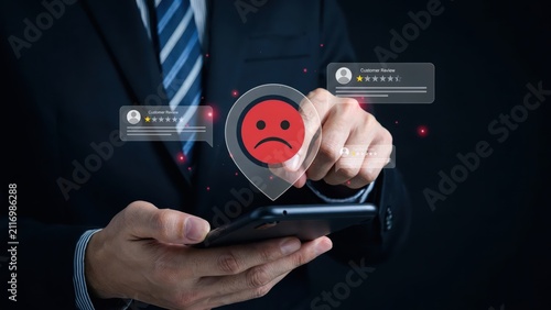Businessman holding smartphone with bad customer review and sad face icon feedback