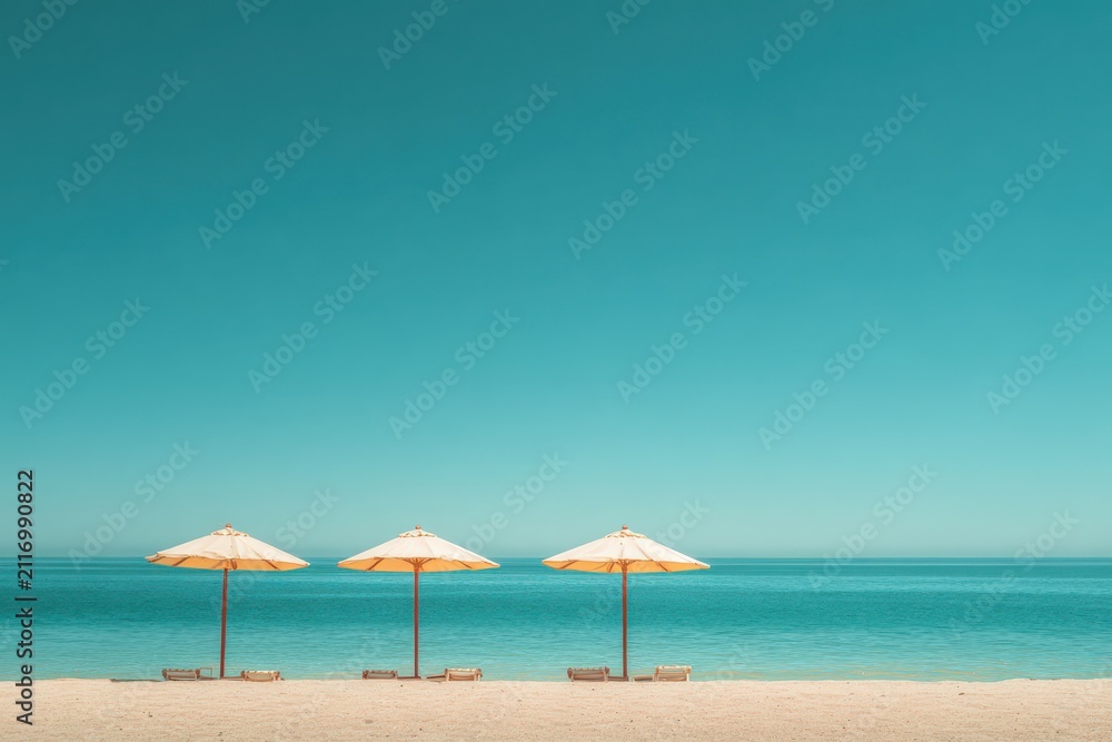 Fototapeta premium Three Open Straw Beach Umbrellas on Empty Sandy Shore with Clear Blue Ocean Horizon
